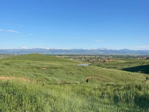 A singletrack berm curving through green grass at Sunset Open Space in early summer, with the snow-capped Front Range beyond.