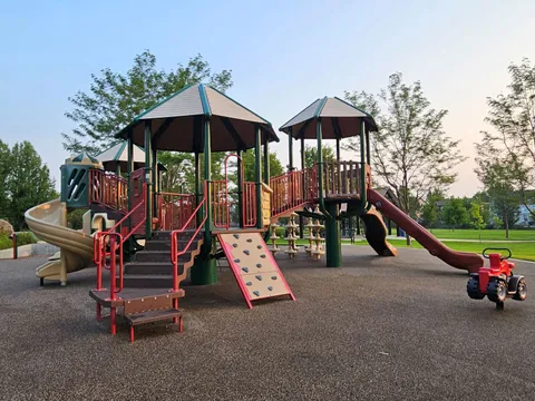 Lehigh Park's playground: twin canopied towers, a spiral slide, a climbing wall and a red slide on a rubber surface