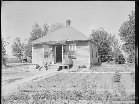 A miner's frame house with a hipped roof and brick chimney at Puritan Camp in 1946, a vegetable garden planted in front