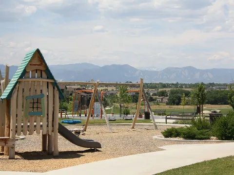 The wooden treehouse playground at Serene Park, swings behind it and the Flatirons and the Front Range on the horizon