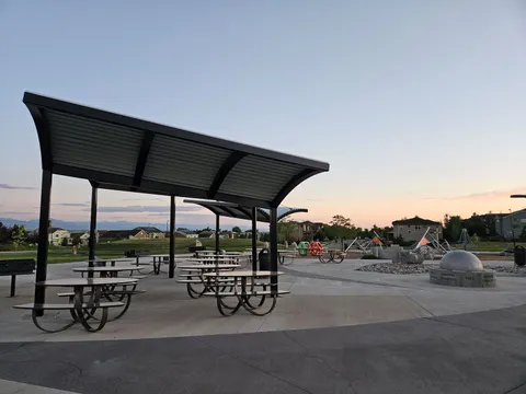 The shelter at Star Meadows Park at dusk, with the moon-phase sundial sphere and the climbing structures beyond